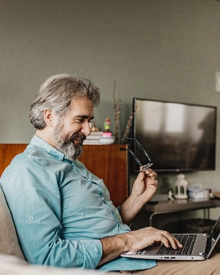 Ein Mann erledigt Zuhause im Wohnzimmer seine Rechnungen mit dem Laptop.